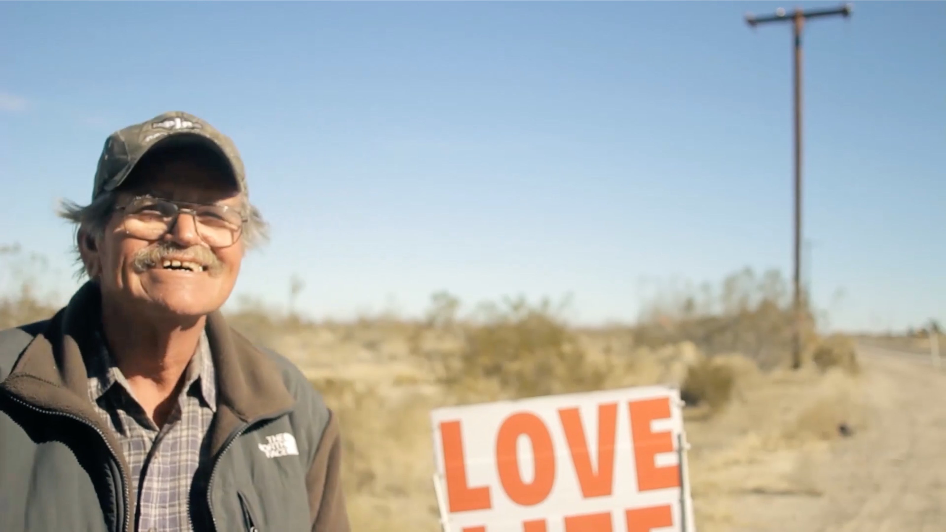 He is seventy-eight years old. He has crossed the United States nine times on foot, fifty-one thousand miles in a quarter of a century, carrying a sign that says LOVE LIFE. He buried his son in 1999 and his daughter in 2005. The walking is not what he is doing. The walking is what holds him up while he does it.